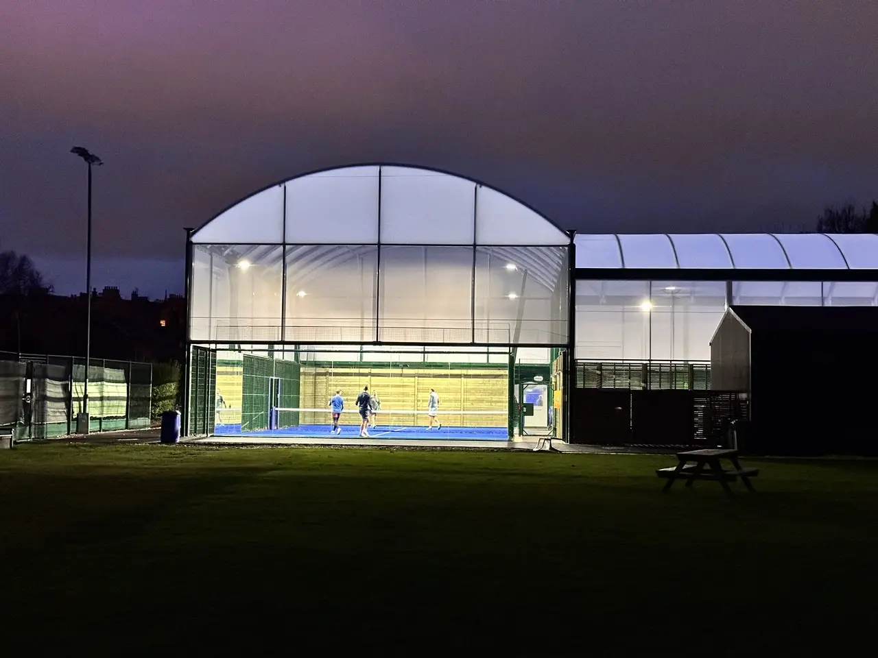 Players visible through the glass walls of The Grange Club padel court, Edinburgh, evening session