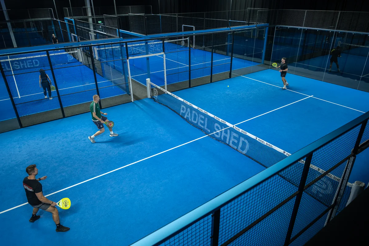 Four players mid-rally on the blue courts at Padel Shed Huddersfield